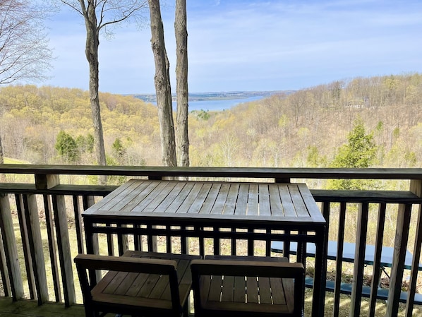 A wooden deck with a table and two benches, overlooking a forested landscape and a body of water.