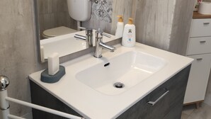 A modern bathroom with a white sink, dark cabinet, and patterned tile backsplash. - Apartment near the sea (Lido di Ostia)