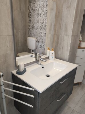 Une salle de bain moderne avec un lavabo blanc, un meuble sombre et un pare-feu en carreaux à motifs.