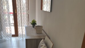 A modern room with a white chair, a wooden desk, a small potted plant, and a patterned curtain. - Apartment near the sea (Lido di Ostia)