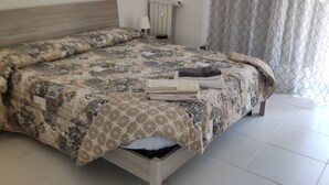 A bedroom with a bed, a radiator, a wall-mounted light, and a window with curtains. - Apartment near the sea (Lido di Ostia)