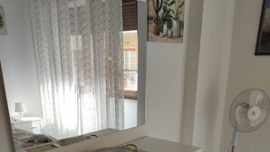 A white dresser with a mirror above it, a small round table with a bowl, and a standing fan to the right. - Apartment near the sea (Lido di Ostia)
