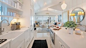 A modern kitchen with white cabinetry, a large island, and a view to the living area. - The Love Shack: Completely restored 1915 direct beachfront cottage! (BRADENTON BEACH)