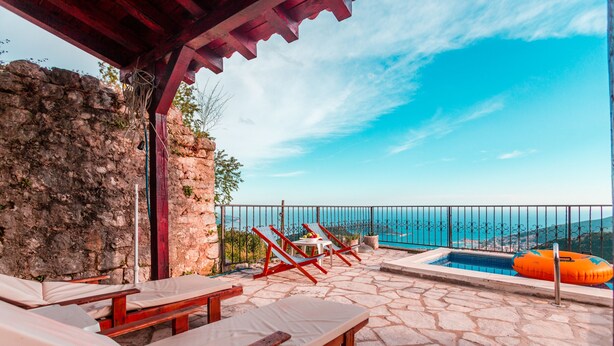 Un patio de piedra con sillones de descanso y una piscina, con vistas a un paisaje pintoresco.