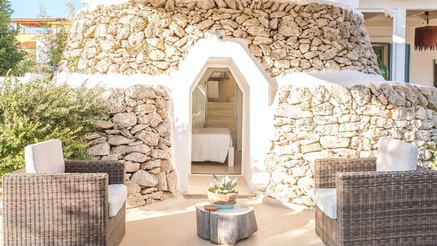 A stone-walled outdoor area with wicker furniture and a small table, leading to a room with a bed. - Villa Paola - Cosy private villa near the sea (Monacizzo-librari-truglione)