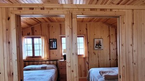 A cabin with two beds, wooden walls, and a window with a curtain. - Superior Reflections Cabin 3 (Schroeder)