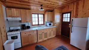 A compact kitchen with wooden cabinets, a stove, a microwave, and a refrigerator. - Superior Reflections Cabin 3 (Schroeder)