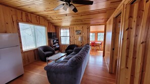 A cabin interior with a wooden interior, a sofa, a television, a dining table, and a ceiling fan. - Superior Reflections Cabin 3 (Schroeder)