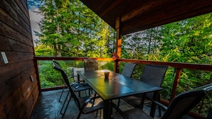 A wooden deck with a table and chairs, overlooking a forested area.