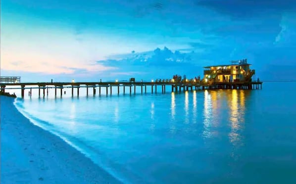 A waterfront property with a pier extending into calm waters, a well-lit building, and a clear sky. - California ranch house (Bradenton)