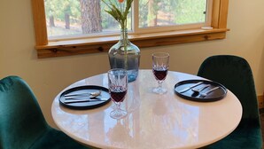 Una mesa redonda con dos sillas, un florero con flores y dos copas de vino tinto.