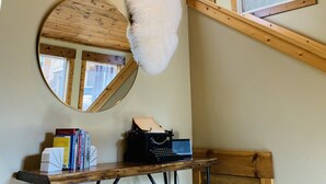 Una habitación con vigas de madera en el techo, un espejo redondo, una máquina de escribir y una ventana con vistas.