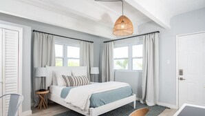 Quarto com cama, mesa de cabeceira, cadeira e janela com cortinas.