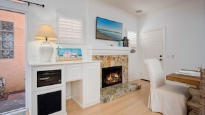 A living room with a fireplace, a dining table with chairs, a lamp, and a painting on the wall. - Lucy's Beach House, (Oceanside)