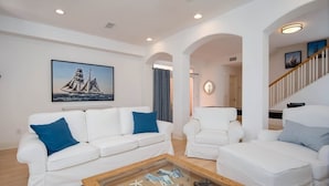 A spacious living room with white sofas, a coffee table with travel photos, and a large sailboat painting on the wall. - Lucy's Beach House, (Oceanside)