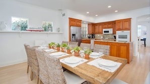 A spacious kitchen with wooden cabinets, a central island, and a dining area with wicker chairs and a wooden table set for six. - Lucy's Beach House, (Oceanside)