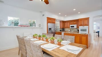 A spacious kitchen with wooden cabinets, a central island, and a dining area with wicker chairs and a wooden table set for six.