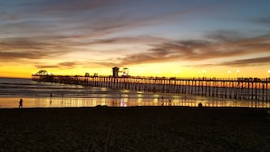 A pier extending into the water with a few people walking along it. - Lucy's Beach House, (Oceanside)