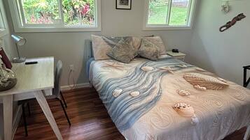 Un dormitorio con cama, escritorio y dos ventanas con vista a vegetación.