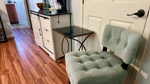 A room with a tufted armchair, a small table, and a kitchen area in the background. - Private Studio, 10 min walk to Hakalau Beach, Hamakau Coast. 15 min to Honoli'i (Hakalau)