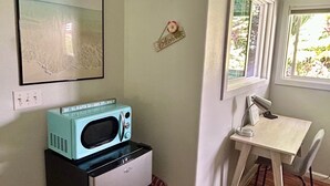 A compact kitchen with a refrigerator, a microwave, and a small table with a chair. There is a window with a view of greenery outside. - Private Studio, 10 min walk to Hakalau Beach, Hamakau Coast. 15 min to Honoli'i (Hakalau)