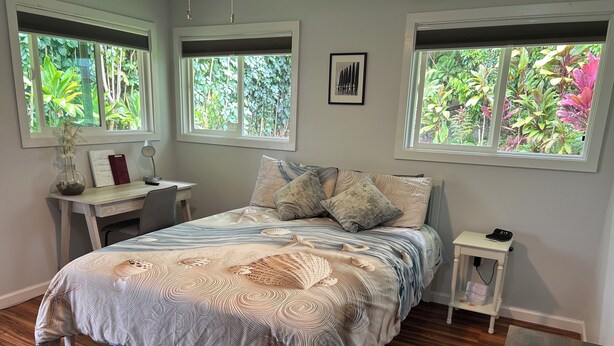 A bedroom with a bed, two windows, a desk, and a nightstand. - Private Studio, 10 min walk to Hakalau Beach, Hamakau Coast. 15 min to Honoli'i (Hakalau)