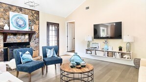 Una sala de estar con pared de piedra, dos sillones azules, una mesa de centro redonda y un televisor de pantalla plana montado en la pared.
