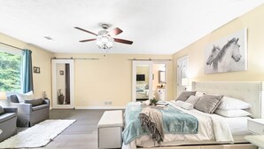 Un dormitorio amplio con una cama grande, un ventilador de techo, vistas al exterior y un baño visible a través de una puerta abierta.