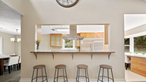 Una cocina moderna con una isla central, taburetes de bar y un ventanal grande.