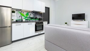 Une cuisine moderne avec des meubles blancs, un réfrigérateur en acier inoxydable et un canapé gris.