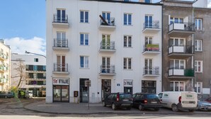 Un immeuble résidentiel à plusieurs étages, doté de balcons, d'une entrée au niveau du sol et d'une enseigne visible indiquant la présence d'un commerce.
