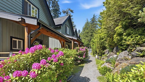 A building with a gravel path, wooden benches, and flowering shrubs.