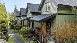A row of green wooden cabins with dark roofs, a gravel path, and surrounding greenery.