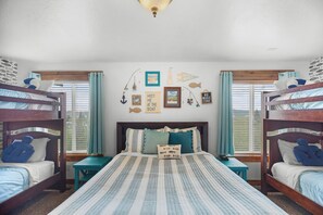 Una habitación con literas, una cama grande con ropa de cama a rayas y decoración de paredes con tema náutico.