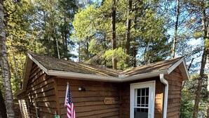 A small wooden cabin with a door and window, surrounded by trees. - Northwoods waterfront Rhinelander Cabin getaway (Rhinelander)