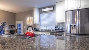A modern kitchen with granite countertops, stainless steel appliances, and a red kettle.
