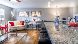 A modern kitchen with a granite countertop, a ceiling fan, and a dining area with a white sofa and red cushions.