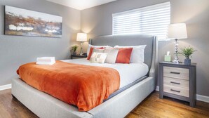 A modern bedroom with a grey upholstered bed, a grey headboard, and a bedside table with a lamp.