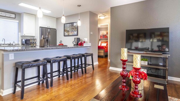 A modern kitchen with a central island, bar stools, a refrigerator, and a dining area with a TV.