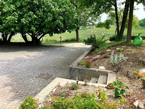 Un camí pavimentat que condueix a una zona de jardí rústica, plena de plantes variades i una petita font.
