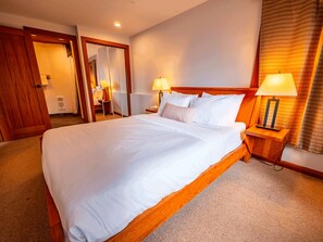Een net opgemaakt bed met witte lakens, een houten hoofdbord en twee bedlampjes.