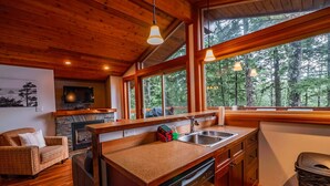 Eine moderne Küche mit Holzschränken, einem Geschirrspüler und einem großen Fenster mit Blick auf einen Wald.