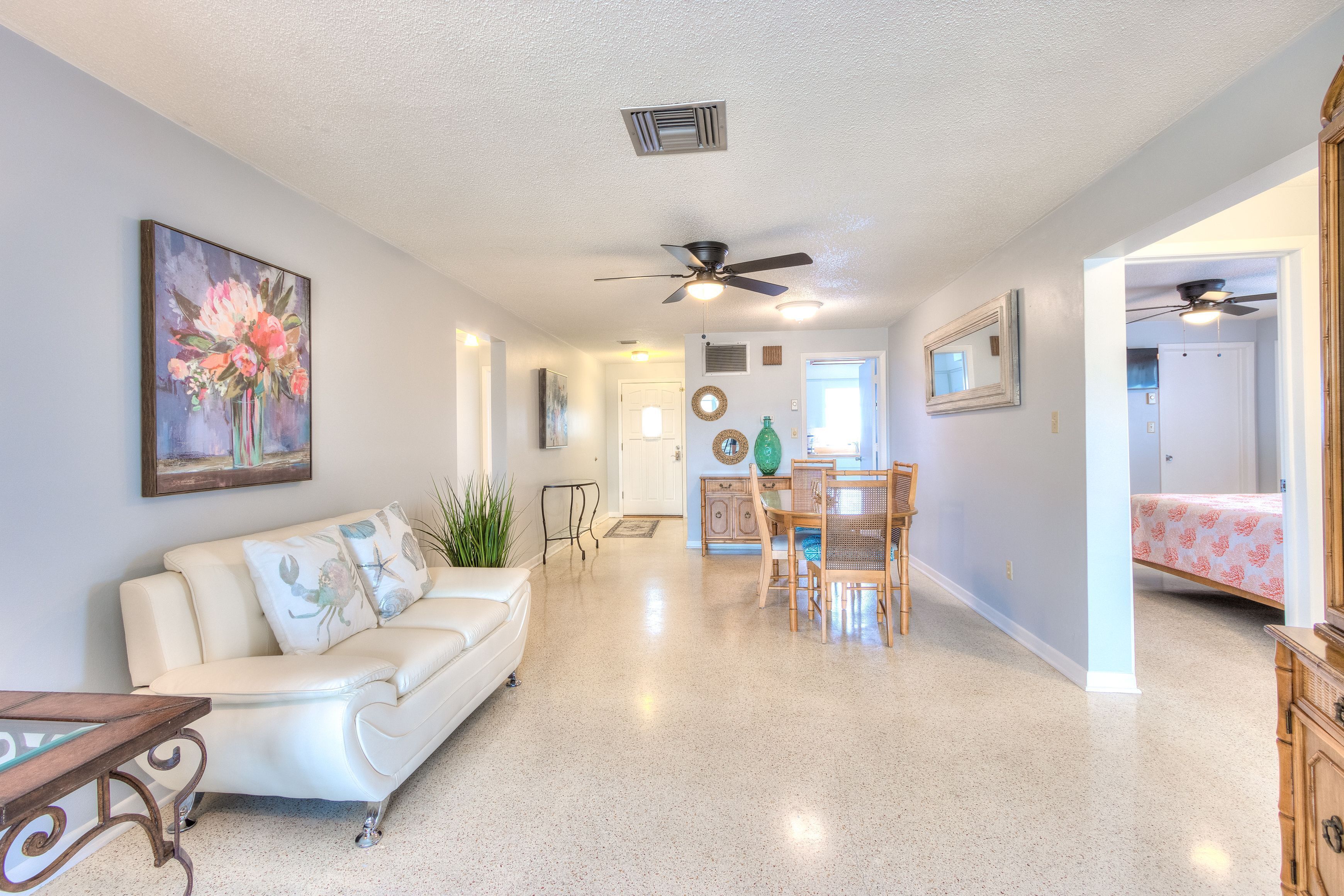 A spacious living room with a white sofa, a dining table with chairs, and a ceiling fan.