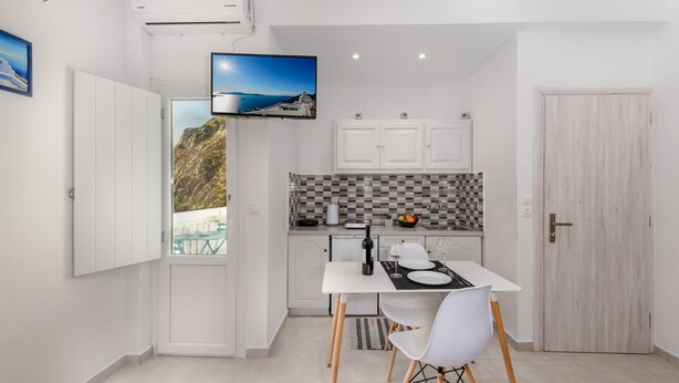 A compact kitchen with white cabinets, a checkered backsplash, and a dining area with a table and chairs. - Aislin House: Where Beachfront Bliss Meets Santorini Charm! (Santorini)