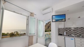 A room with a view of the sea, a TV mounted on the wall, and a kitchenette with a tiled backsplash. - Aislin House: Where Beachfront Bliss Meets Santorini Charm! (Santorini)
