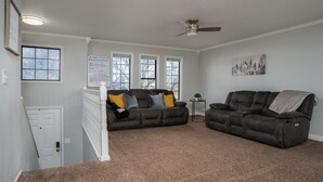 A living room with a brown carpet, two dark brown sofas, a ceiling fan, and a white door.