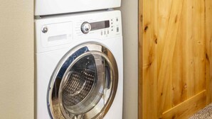 A laundry area with two stacked front-loading washing machines and a wooden sliding door. - Best Views Street (Colorado Springs)