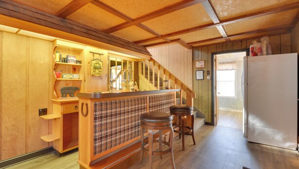 Um interior em madeira com área de bar, banquetes, geladeira e escada.