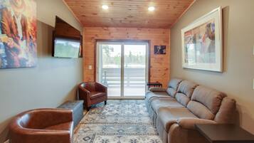 Una habitación con techo de madera, un ventanal grande, un sillón de cuero marrón, un sofá color beige y un tapete estampado.