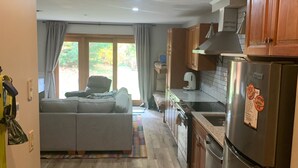 A compact kitchen with wooden cabinets, a stainless steel refrigerator, and a dining area with a window view. - Sugarloaf Ski-In/Ski-Out Condo – Golf, Bike & Hike (Carrabassett valley)